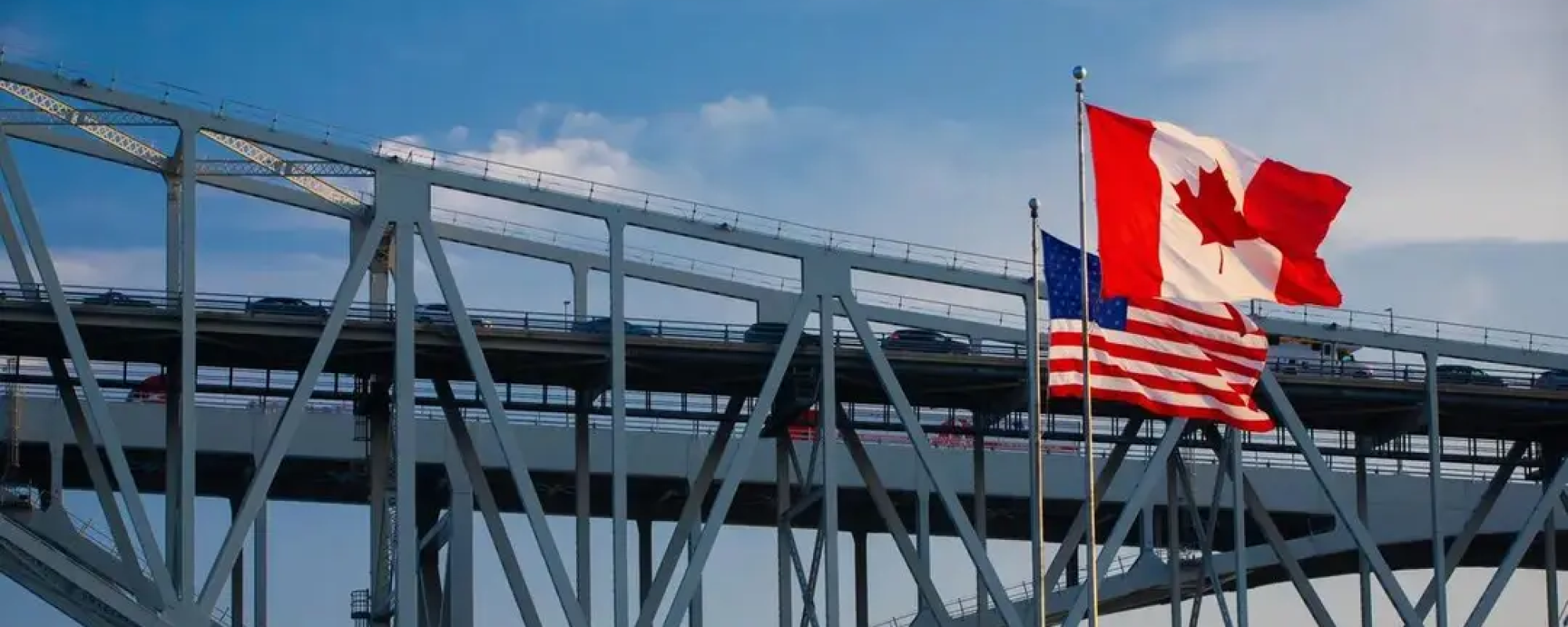 Canadian and American flags in front of a bridge.