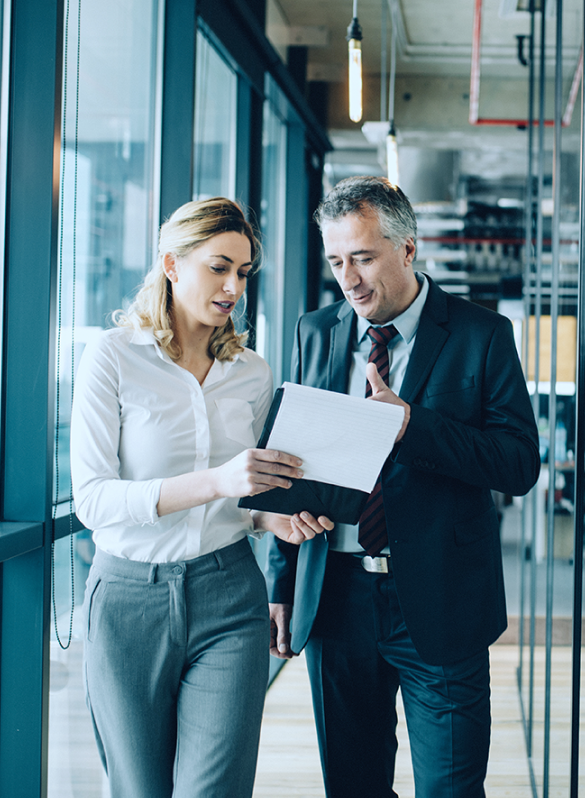 man and woman walking down office hallway looking at documents