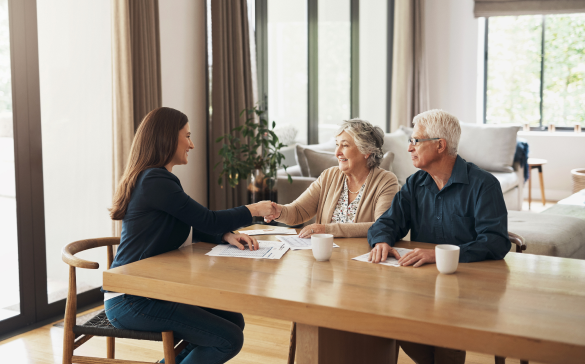 elderly couple sit at table shaking hands with lady sitting across from them