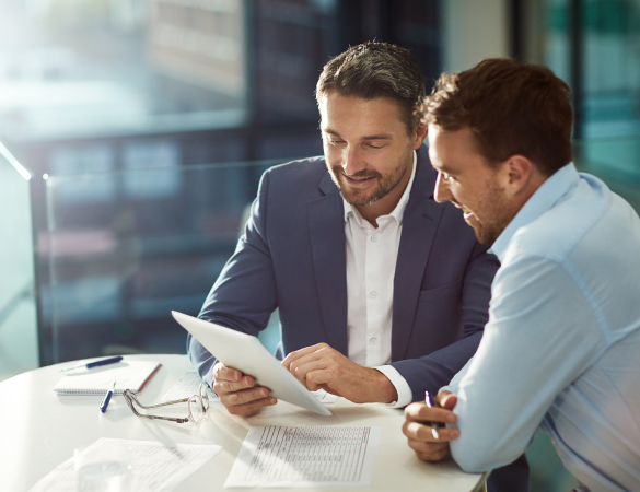 two men sit at a table looking over documents