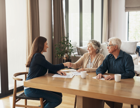 elderly couple sit at table shaking hands with lady sitting across from them