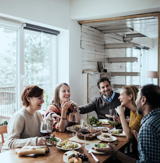 5 people sitting around table eating and laughing