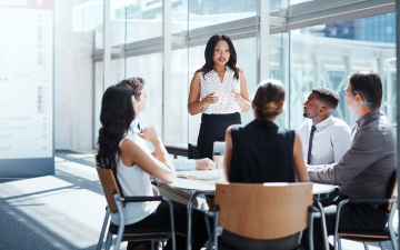 business professionals sitting around a table listening to a lady speaking