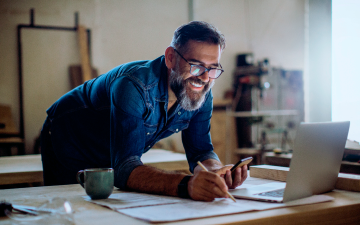 man leaning over desk looking at his phone