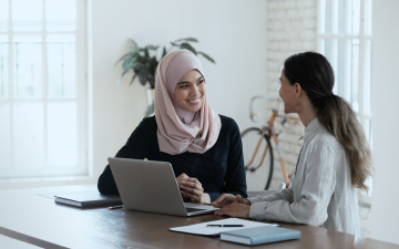 two girls sitting by a laptop and talking