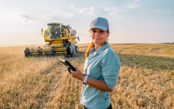 woman standing in grain field in front of large yellow tractor