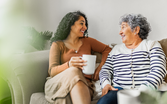 two women sit on a couple holding coffee mugs