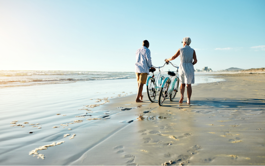 man and woman push a bicycle along the beach