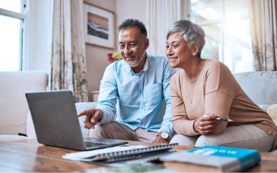 man and woman sitting on couch looking at open laptop