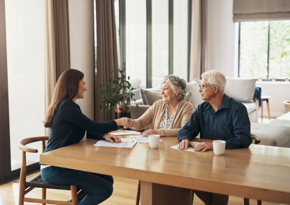 elderly couple shake hands with lady across the table