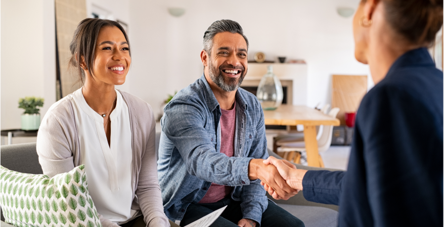 man and woman sitting on couch shaking hands with woman in suit