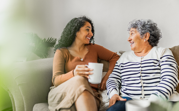 two women sit on a couch drinking coffee