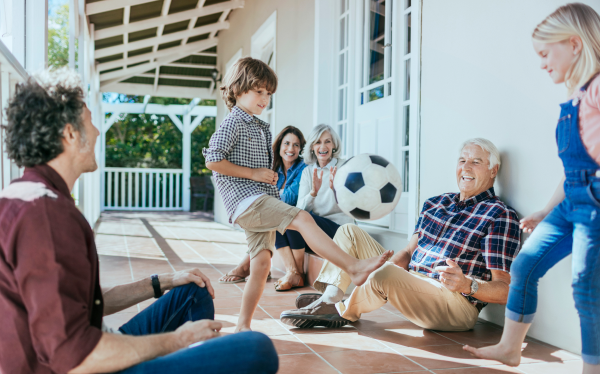 family sitting on a porch watching a child kick a soccer ball