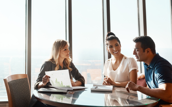 woman and man sitting at table speaking to a lady holding documents