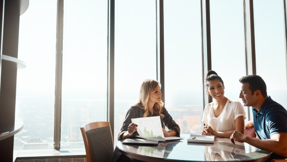 man and woman sitting at a table speaking to lady holding a document